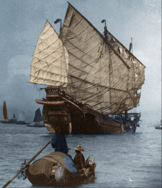 Vintage black and white photograph of a large sailing ship on water with smaller boats in the background.